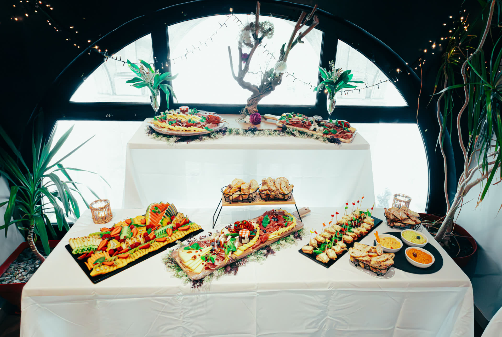 Grazing tables of charcuterie, cheeses, fruit and bread before an arched window