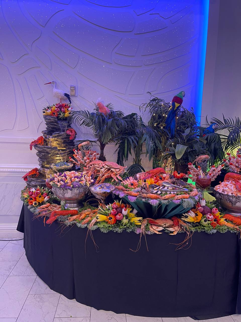 Grand seafood display with lobster, crab and shrimp beside a cascading fountain and tropical florals