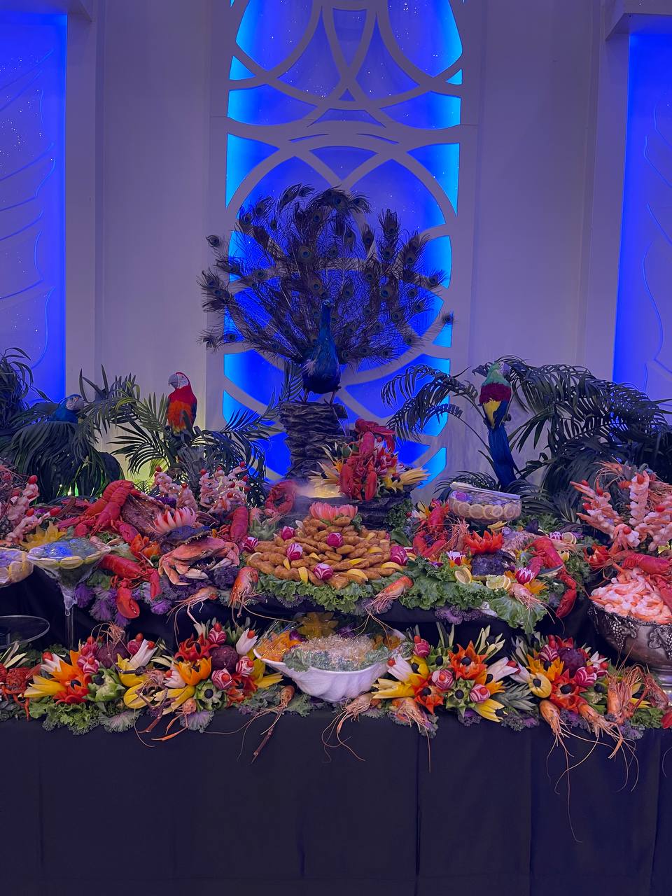 Elaborate seafood buffet crowned by a peacock display, with carved fruit flowers and iced shellfish