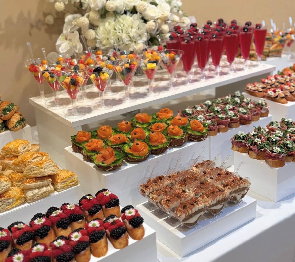 Reception table with fruit cups, salmon cucumber bites, berry toasts and tiramisu verrines