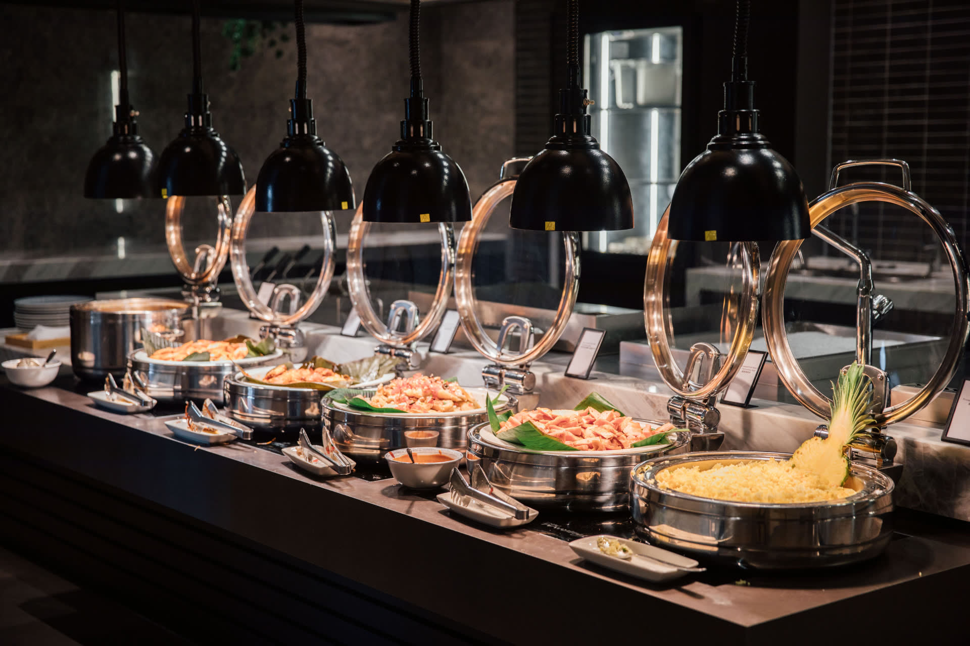 Chef-attended hot station with polished chafing dishes under warming lamps